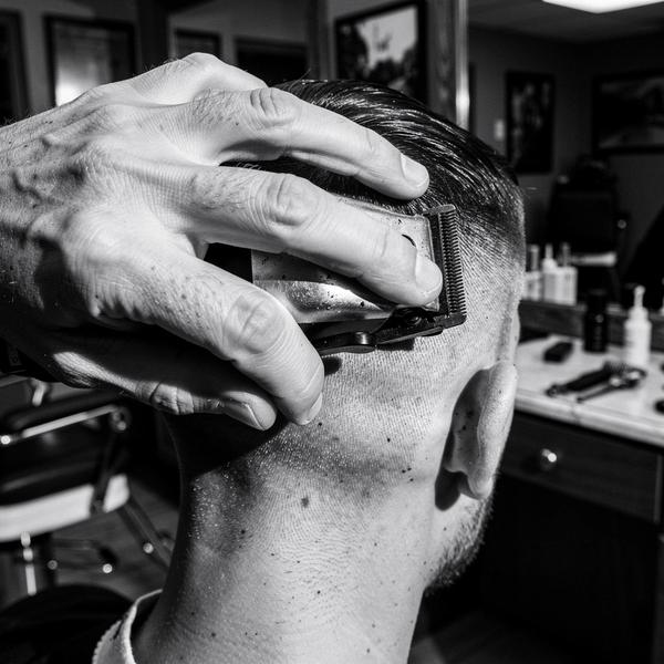 Barber's hands mid-cut with clippers against a neckline